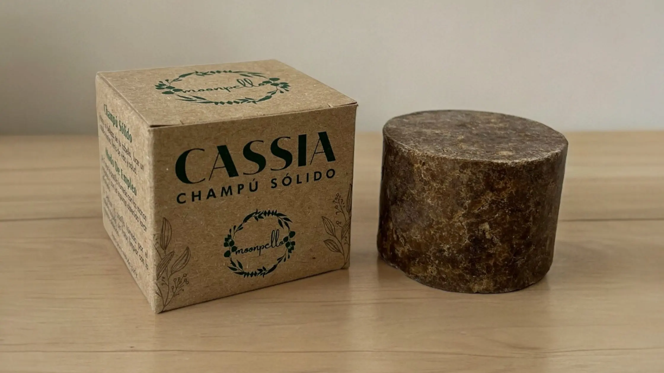 Champú sólido natural Moonpello – Cassia fortalecedora Champú sólido natural de Cassia de Moonpello junto a su caja sobre una mesa de madera.